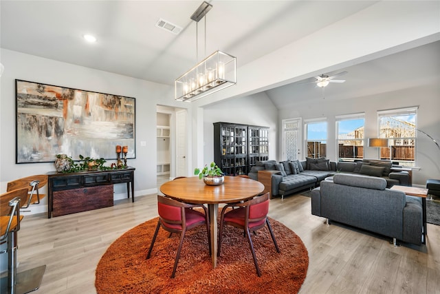 dining room with light hardwood / wood-style floors, built in shelves, ceiling fan with notable chandelier, and vaulted ceiling