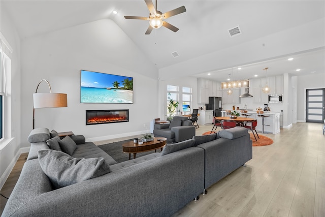 living room featuring light hardwood / wood-style floors, high vaulted ceiling, sink, and ceiling fan