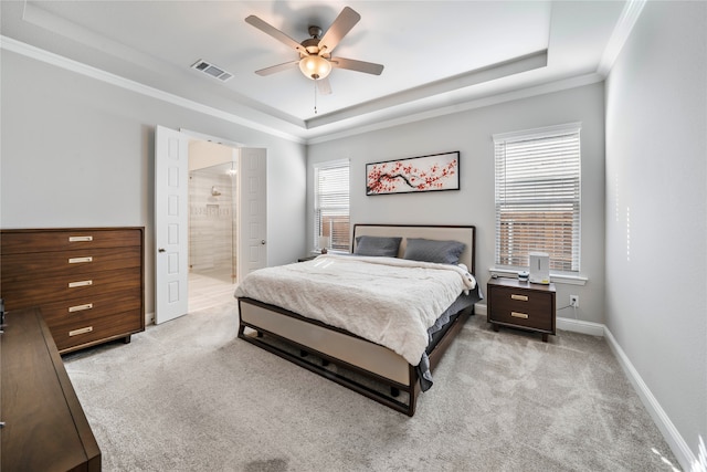 bedroom featuring a raised ceiling, ceiling fan, light carpet, connected bathroom, and crown molding