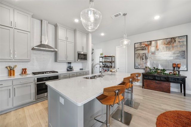 kitchen featuring wall chimney exhaust hood, appliances with stainless steel finishes, sink, and an island with sink