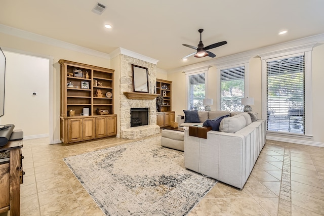 living room featuring light tile patterned floors, ceiling fan, built in shelves, a stone fireplace, and crown molding