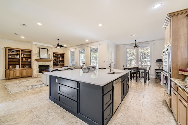 kitchen featuring appliances with stainless steel finishes, a kitchen island with sink, ornamental molding, a stone fireplace, and sink