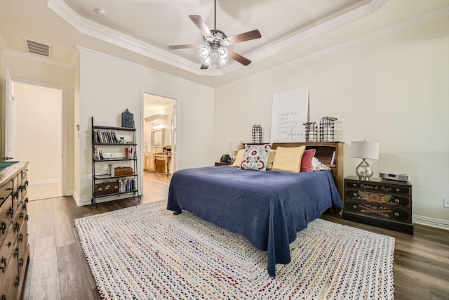 bedroom with ensuite bath, dark wood-type flooring, a raised ceiling, and ceiling fan