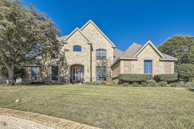 french provincial home with a front lawn, brick siding, stone siding, and a shingled roof
