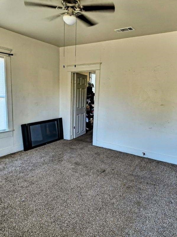 unfurnished living room featuring ceiling fan and dark colored carpet