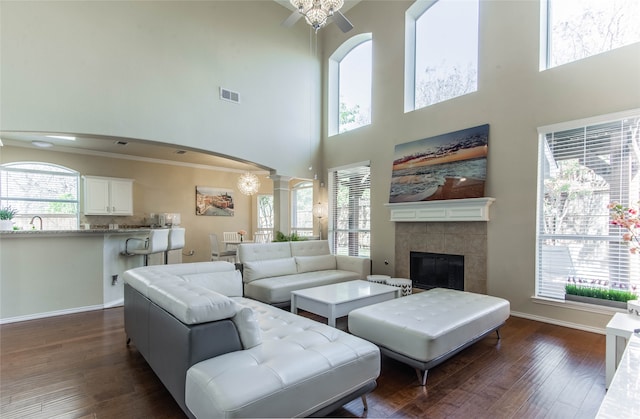 living room featuring a high ceiling, ornate columns, dark hardwood / wood-style floors, a fireplace, and ceiling fan