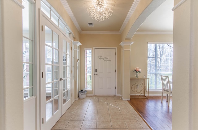 entryway with ornate columns, a notable chandelier, ornamental molding, and light wood-type flooring