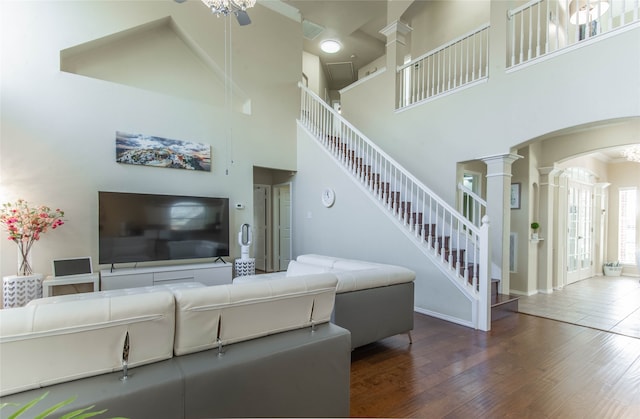 living room with ceiling fan, ornate columns, a high ceiling, and dark hardwood / wood-style flooring