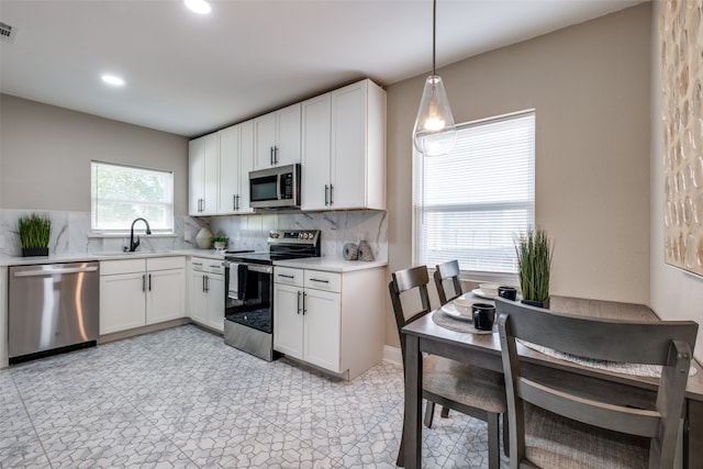 kitchen featuring white cabinetry, stainless steel appliances, decorative light fixtures, and sink