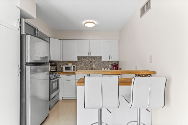 kitchen featuring tasteful backsplash, butcher block countertops, white cabinetry, stainless steel appliances, and light tile patterned floors