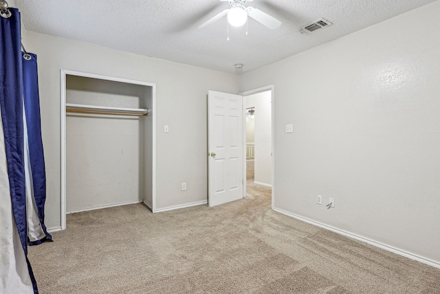 unfurnished bedroom featuring a closet, a textured ceiling, light colored carpet, and ceiling fan