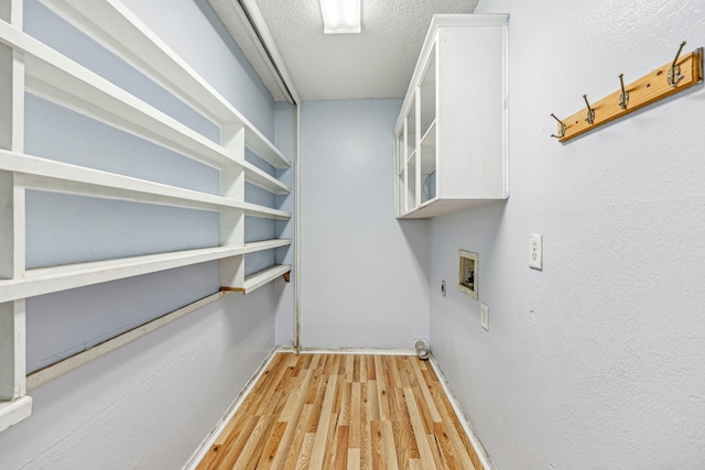 clothes washing area with washer hookup, a textured ceiling, hookup for an electric dryer, and light hardwood / wood-style flooring