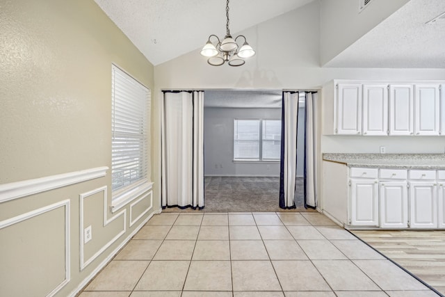 unfurnished dining area featuring light tile patterned flooring, a wealth of natural light, a chandelier, and lofted ceiling