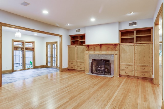 unfurnished living room with a fireplace, light hardwood / wood-style flooring, built in features, and french doors