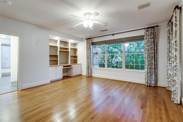 unfurnished living room with ceiling fan, built in desk, and light hardwood / wood-style floors