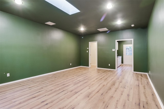 spare room featuring a skylight and light hardwood / wood-style floors