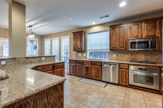 kitchen featuring stainless steel appliances, light stone counters, backsplash, decorative light fixtures, and light tile patterned floors