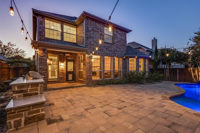 back house at dusk with a fenced in pool, area for grilling, and a patio