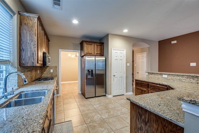 kitchen with sink, tasteful backsplash, light stone counters, light tile patterned floors, and appliances with stainless steel finishes