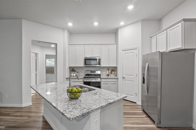 kitchen featuring light hardwood / wood-style floors, white cabinets, stainless steel appliances, and an island with sink