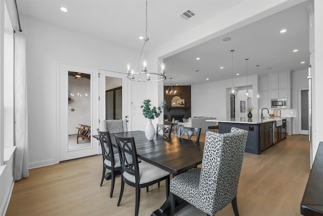 dining space with a large fireplace, a notable chandelier, and light hardwood / wood-style floors