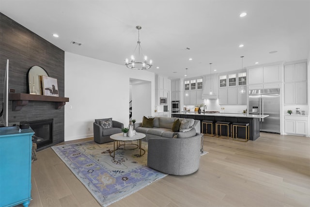 living room with sink, light hardwood / wood-style floors, an inviting chandelier, and a fireplace