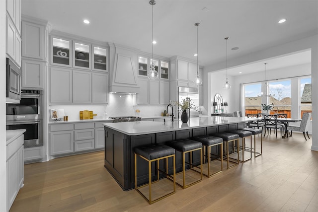 kitchen featuring light hardwood / wood-style floors, a breakfast bar, premium range hood, and a large island with sink