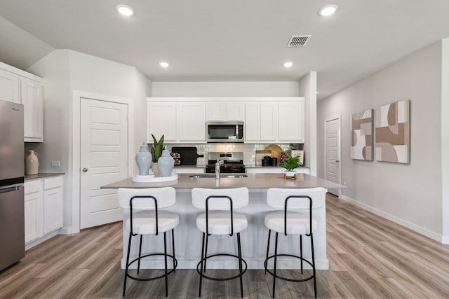 kitchen featuring white cabinets, stainless steel appliances, and an island with sink