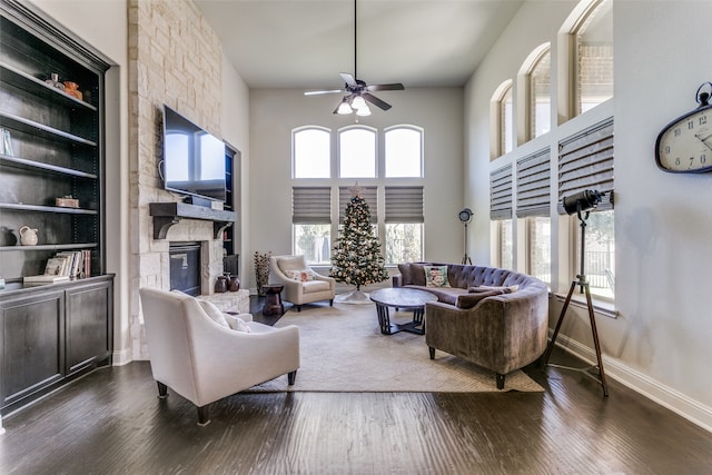 living room with built in shelves, ceiling fan, dark wood-type flooring, a fireplace, and a high ceiling