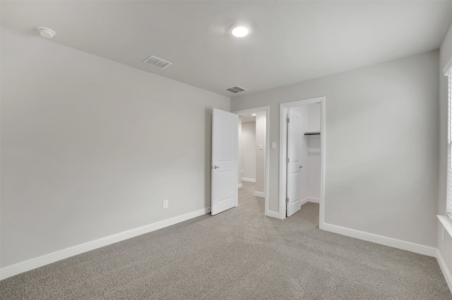 unfurnished bedroom featuring a closet, light carpet, and a walk in closet