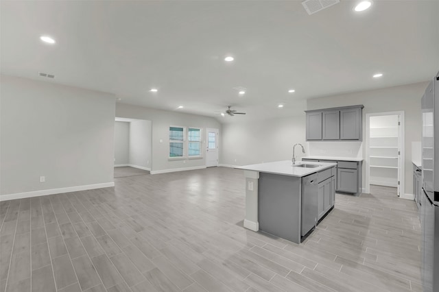 kitchen featuring an island with sink, light hardwood / wood-style flooring, gray cabinetry, sink, and stainless steel dishwasher