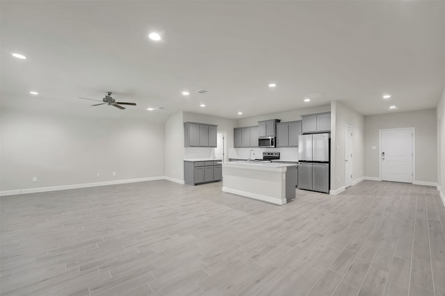 kitchen featuring appliances with stainless steel finishes, light hardwood / wood-style flooring, gray cabinetry, and an island with sink