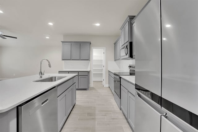 kitchen featuring a kitchen island with sink, stainless steel appliances, sink, and gray cabinetry