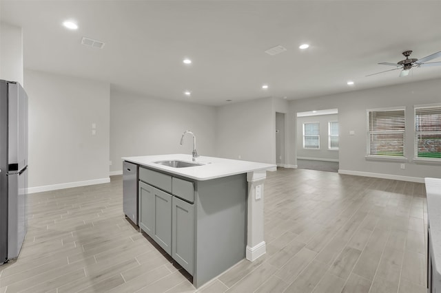 kitchen with appliances with stainless steel finishes, a kitchen island with sink, light wood-type flooring, gray cabinets, and sink