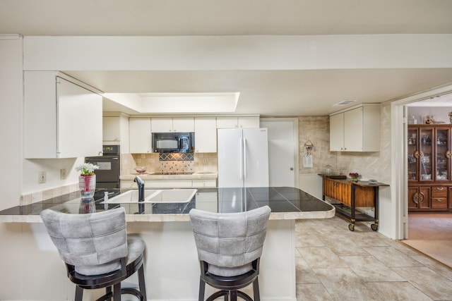 kitchen with kitchen peninsula, sink, black appliances, a kitchen bar, and white cabinetry