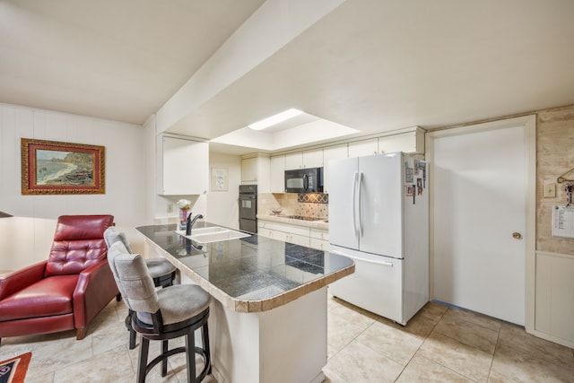 kitchen with kitchen peninsula, sink, black appliances, a kitchen bar, and white cabinetry