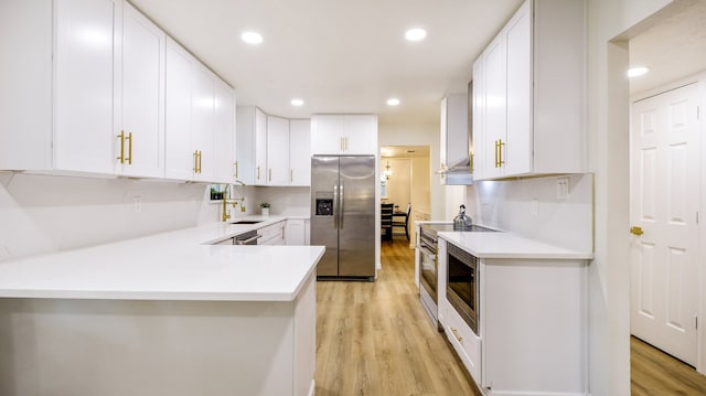 kitchen featuring appliances with stainless steel finishes, kitchen peninsula, white cabinets, and light hardwood / wood-style floors