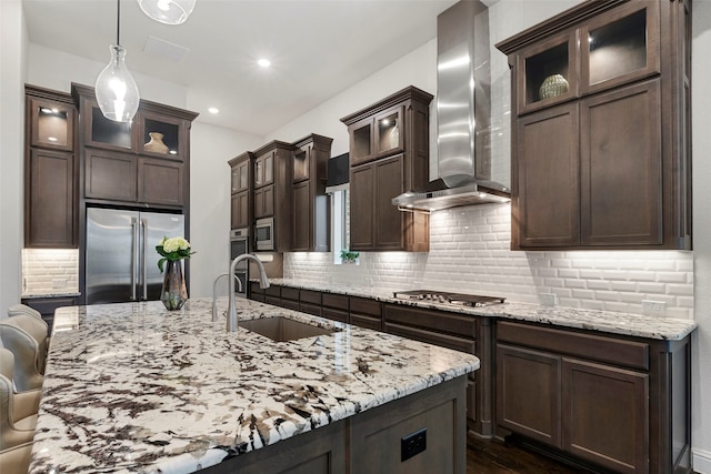 kitchen featuring light stone countertops, sink, stainless steel appliances, wall chimney exhaust hood, and decorative light fixtures