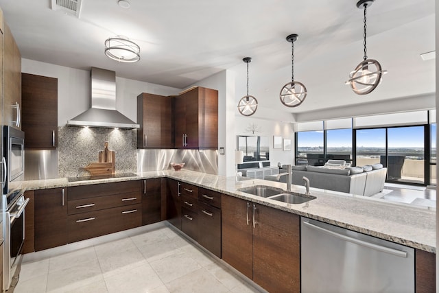 kitchen featuring wall chimney range hood, hanging light fixtures, sink, appliances with stainless steel finishes, and tasteful backsplash