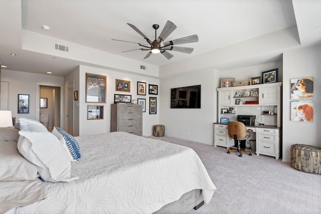 carpeted bedroom featuring built in desk, ceiling fan, and a raised ceiling