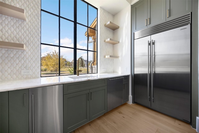 kitchen with sink, black dishwasher, stainless steel built in fridge, light hardwood / wood-style floors, and decorative backsplash