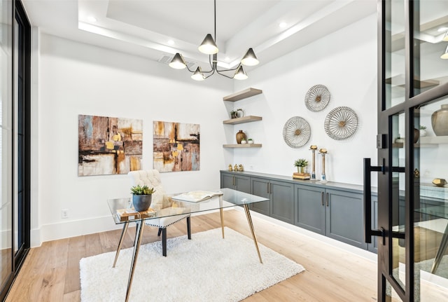 office area with an inviting chandelier, light wood-type flooring, and a tray ceiling