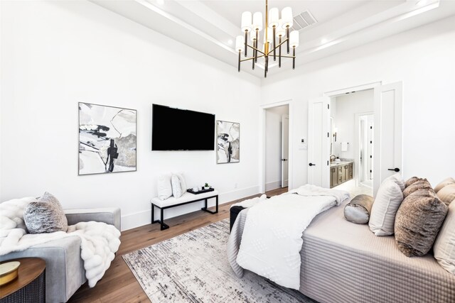 bedroom featuring a tray ceiling, wood-type flooring, a chandelier, and ensuite bathroom