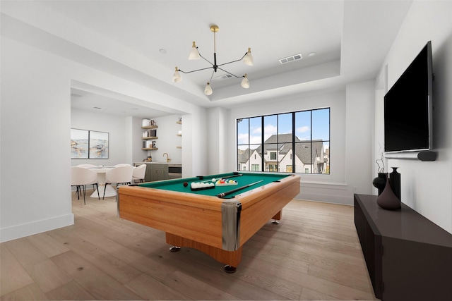 rec room featuring a notable chandelier, pool table, light hardwood / wood-style flooring, and a raised ceiling