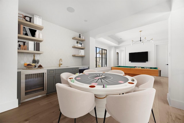 dining room featuring an inviting chandelier, indoor wet bar, light hardwood / wood-style flooring, a tray ceiling, and beverage cooler