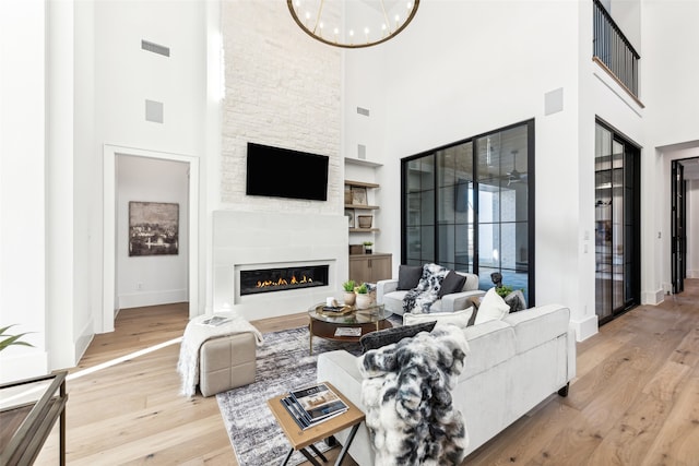 living room featuring a stone fireplace, a towering ceiling, and light hardwood / wood-style flooring