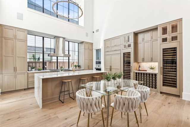 dining area with wine cooler, sink, light hardwood / wood-style floors, and a high ceiling