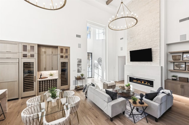 living room featuring wine cooler, a notable chandelier, a fireplace, and a high ceiling