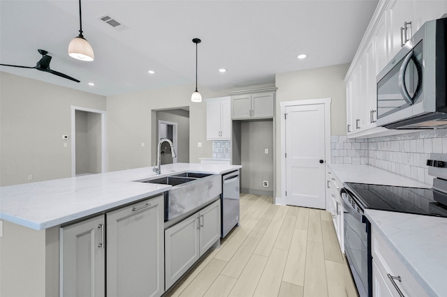 kitchen with backsplash, stainless steel appliances, decorative light fixtures, a center island with sink, and white cabinets