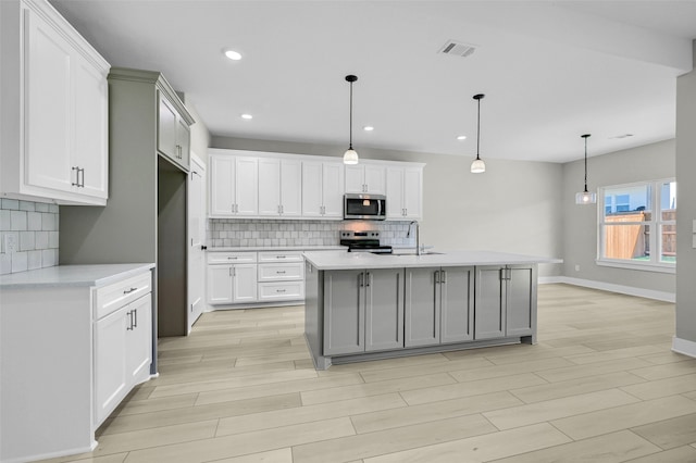 kitchen with stainless steel appliances, white cabinetry, hanging light fixtures, and a center island with sink